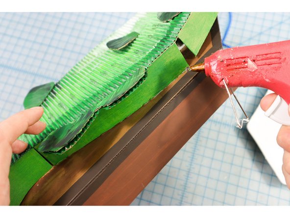 With the motors in place and the angles set, use hot glue to attach the center part of the fish body to the plaque. Remove any excess glue with tweezers.