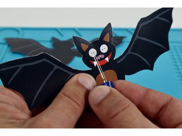 Thread each LED through a pair of holes taking care to orient the LED legs as pictured with the shorter legs toward the outer edges and the long legs through the inner holes nearest the bat's nose.