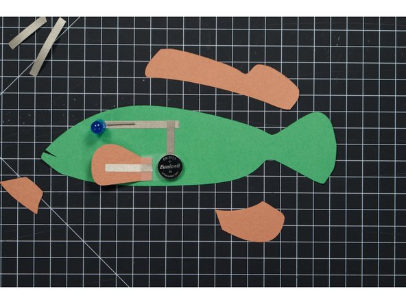 Add a piece of Maker Tape to the fin as shown. It should line up with the battery so it will make contact when the fin is folded over. This is our switch, which completes the circuit, allowing current to flow.