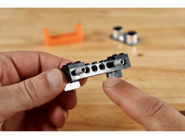 Connect 2 of your (2x2) 90 degree brackets to the outside edges of a (1x8) technic brick with holes to create the build shown in slide 1.