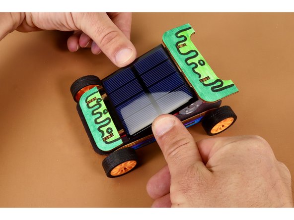 With foam tape peeled and stuck in place, connect the red motor wire to the red solar panel wire and the black motor wire to the black solar panel wire. With wires connected, press solar panel into place as shown with dark purple, glossy side facing UP.