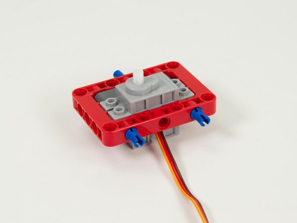 Place two long blue pins into the holes on the back of the red frame as shown.