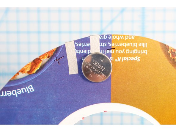 Make a loop of Maker Tape small enough to fit inside the black ring on the negative side of the battery, and stick it on. Place the ring and battery on the negative piece of tape.