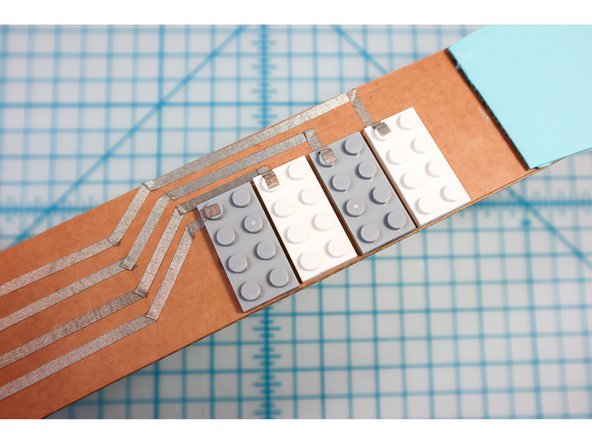 Carefully lay the maker tape according to the neck template, connecting each string to the left peg of each LEGO. Make sure the tapes don't touch each other.