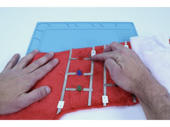 Stick half of each individual piece of Maker Tape that you prepared to an LED leg and fold over back on itself to stick the sticky sides together.  This effectively sandwiches each LED leg between Maker Tape and will keep fuzz off the legs while also increasing the contact area for the next pieces of tape to be placed.