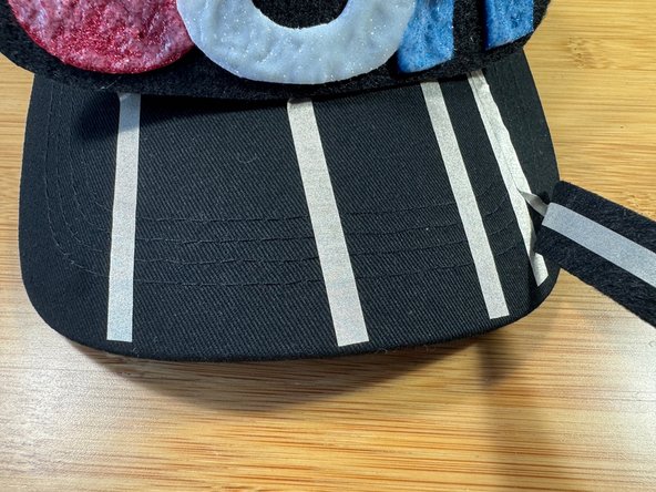 Stick the Maker Tape tails coming from &quot;U&quot;, &quot;S&quot;, and &quot;A&quot;, to the hat as shown and trim any excess.