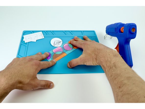 Use a hot glue gun to place hot glue on the inside of a frame while pressing the colored rectangle into place on top. Be sure to be accurate with your placement as each edge will eventually need to be fastened to the next. Overhang can make this tricky.