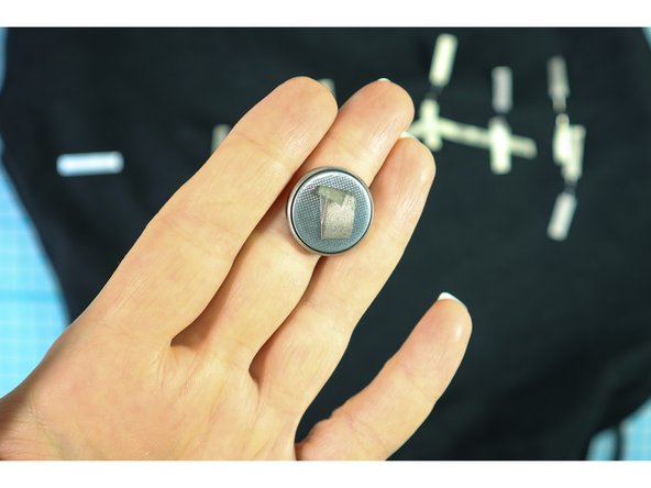 Make a small loop of Maker Tape with the adhesive facing out, and stick it to the battery on the negative side. Be sure that the loop doesn't go outside the black ring.