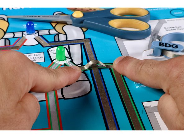 Measure, cut, peel, and stick the first Maker Tape path shown. It should lead from the Black Negative (-) Path coming out of the control box, up toward the Green LED.