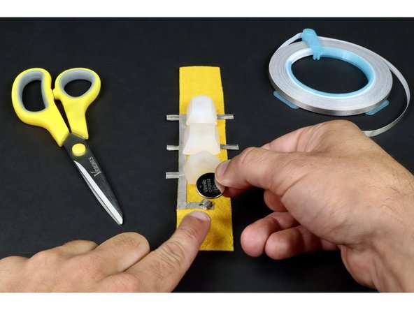 Stick your CR2032 battery to the tape loop with the positive side of the battery faced UP.