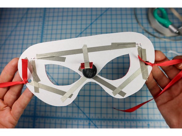 Tie a ribbon that's long enough to tie behind the wearer's head to the hole on each side.