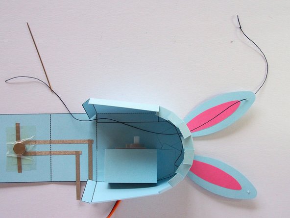 Using the sewing needle, sew a piece of thread through the hole in the ear and then the hole in the body