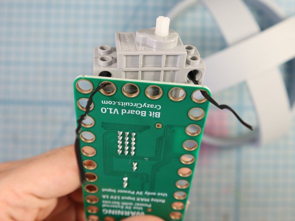 Use a plastic-covered twist tie to attach the servo motor through the GND and 3V holes.