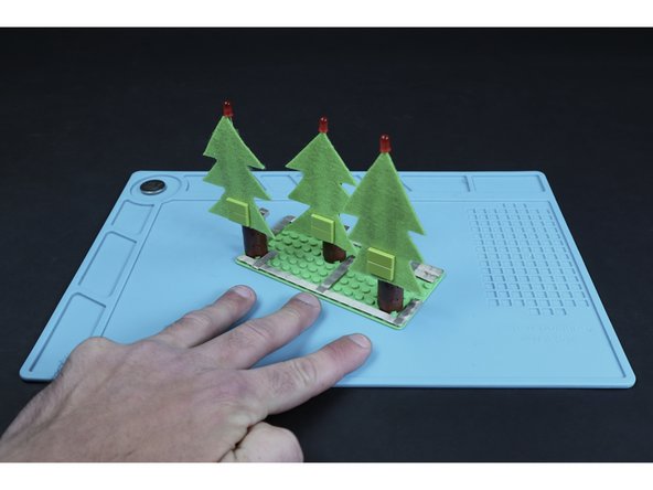 Measure/cut 3 small tape segments and press them into place where shown in image 2 so that they connect to the long path you just made and lead to/end at the right side of each of the three trunks (when viewed from the front).