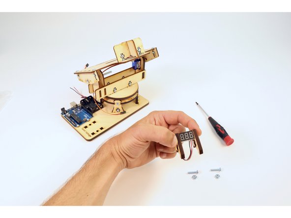 Fit the side tabs of the voltmeter into the slots on the wooden brackets and pinch together as shown in the second photo.