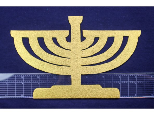 Do not place hot glue along the top edge of the menorah to allow the candles to tuck underneath it in a later step.