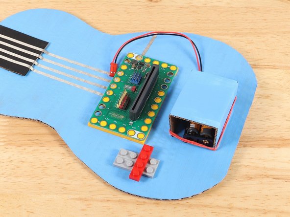 Add the LEGO plates to the guitar body. This should go on the opposite side of the Bit Board from the ground pathway. We will be connecting the Potentiometer to Pin 0 so we need to keep it close by.