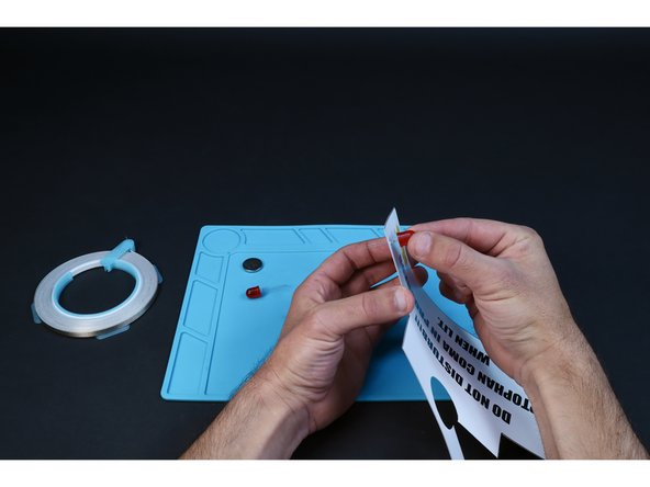 Each of the pairs of holes you just poked is for a single LED. From the front, thread the legs of each of your two LEDs into one of those pairs of small holes. Take care to insert the long LED legs into the upper holes and the shorter LED legs into the bottom holes.