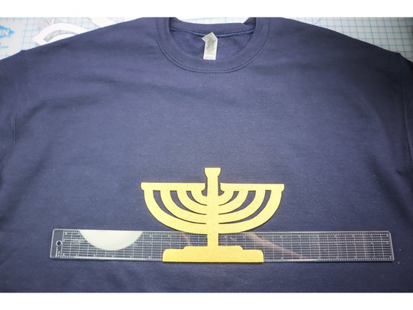 Measure the center of the sweatshirt and hot glue the menorah in place, making sure there is enough room for the candles and LEDs.