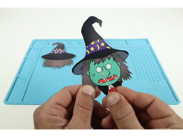 Thread each LED through a pair of holes taking care to orient the LED legs as pictured with the shorter legs toward the outer edges and the long legs through the inner holes nearest the witch's nose.