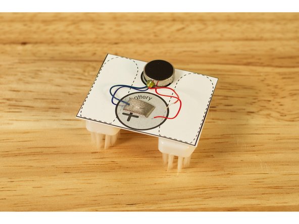 Roll the tape into a loop and stick it down to the template, and then press the blue motor wire into the tape.