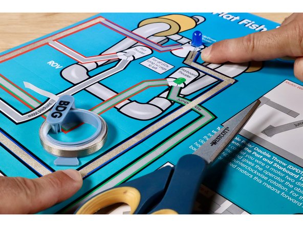 Measure, cut, peel, and stick the Maker Tape paths shown to complete the Blue LED/ROV outcome path. It should lead from the black/blue branch coming out of the control box, up to the short Negative (-) Leg of the Blue LED, then out the Long Positive (+) Leg of the Blue LED,  and back to the Red Positive (+) Path leading back to the battery.