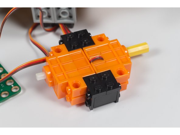 Connect two of the brackets to a 2x2 LEGO brick as shown. Make two of these assemblies and use them to connect the servo motors back to back.