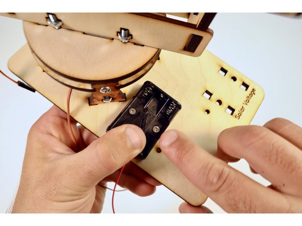 Position the battery pack as pictured and thread the two screws through the two holes as well as the wooden plate below.
