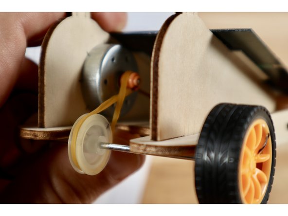 Change the direction the motor spins by putting a twist in the rubber band that connects the orange driver pulley wheel to the white follower pulley wheel.