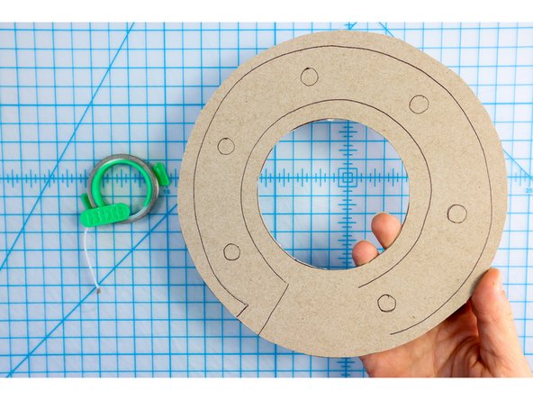 Stick two paths of maker tape to the cardboard. One will start on the back and go around the outside of the LED markers. The other will start about one inch from the first (also on the back) and go around the inside of the LED markers as shown.