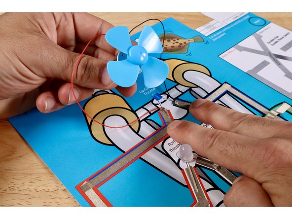 Now pull the motor wires up from their positions on the Green Path and use them to connect where shown atop the Blue LED/ROV Outcome path. If you need to cut two fresh pieces of Maker Tape, do so. The two pushbuttons that previously controlled the Blue LED will now control the motor.