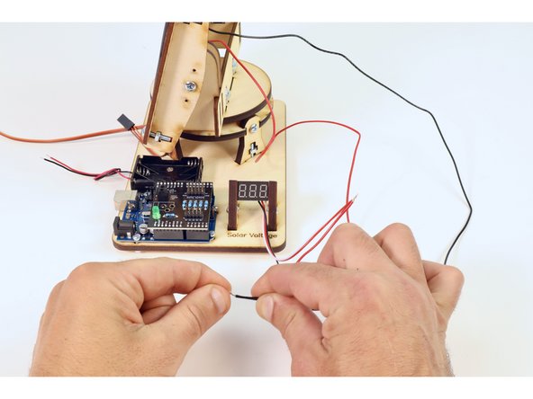 Twist the copper strands from the black wire of the solar panel to those of the black wire of the voltmeter.