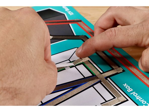 Install the switch by positioning it atop the gap (Maker Tape side down) where shown and securing it with another piece of Maker Tape. The fold should be atop the black horizontal line of the box graphic. The LED will now momentarily light up when the lever is pressed into contact with the upper part of the path across the gap.