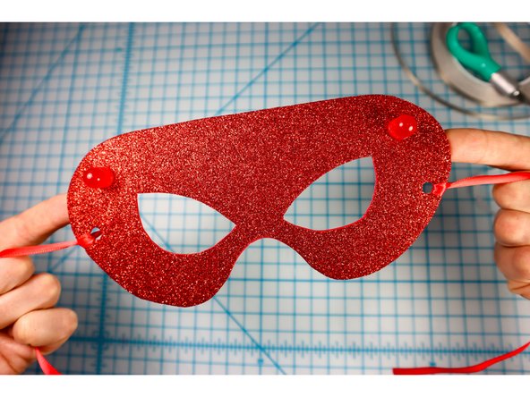 Tie a ribbon that's long enough to tie behind the wearer's head to the hole on each side.