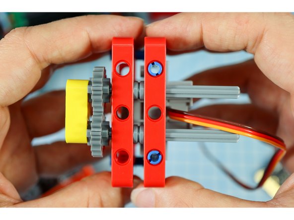 Get the frame piece with the motor attached and connect the two together as shown, with the blue pins on the bottom and the gray axles on the top.