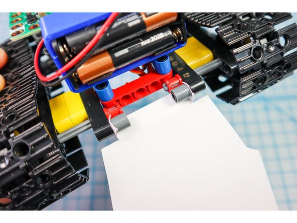 Use two pin/beam sets to connect the paper to the back of the tank under the battery pack where shown.