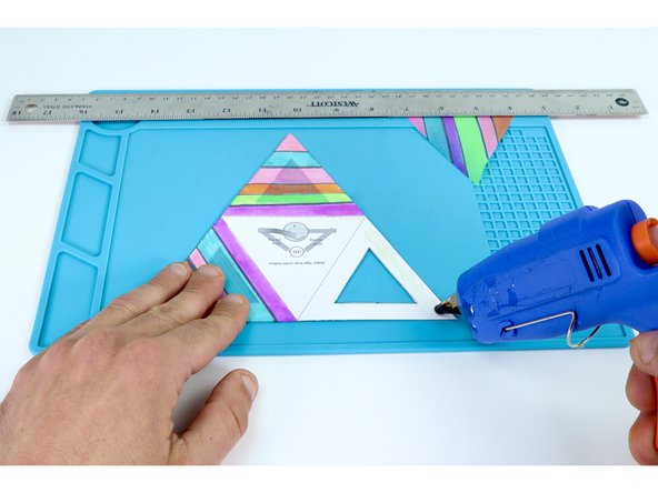 Use a hot glue gun to place hot glue on the inside of a frame while pressing one of the colored triangles into place on top. Be sure to be accurate with your placement as each edge of a given face will eventually need to be fastened to the next. Overhang can make this tricky.  Do this ONE FACE AT A TIME. 