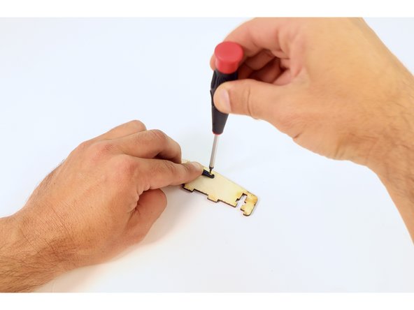 On a flat surface away from the wooden side brace, start one screw in the second hole from the edge on one side of the servo horn. Then, start the other screw in the second hole from the edge of the on opposite side. Turn the screws so their tips are just barely poking out of the back.