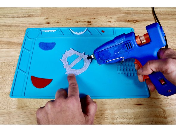 Using a hot glue gun and photo one for reference, squeeze a bead of hot glue around the perimeter of the face and mouth.