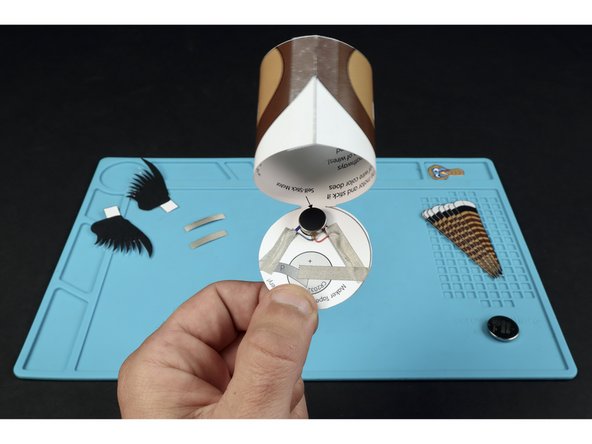 First, use two Maker Tape sections to secure the two motor wires in place. Then, add the Maker Tape section shown so that it sits atop the battery graphic and connects to the tape path leading from the RED wire of the motor.