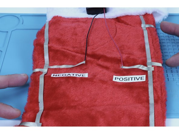 Cut two Maker Tape pieces that can reach from the ends of the (-) paths on the front AROUND the edge to connect to the negative (black) path set up on the back of the stocking.  Peel and stick them into place as shown.