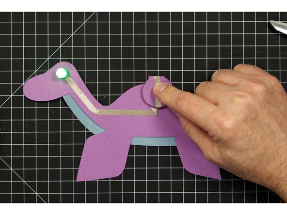 Fold down the round battery holder section on the back so that the positive line of tape make contact with the top of the battery.