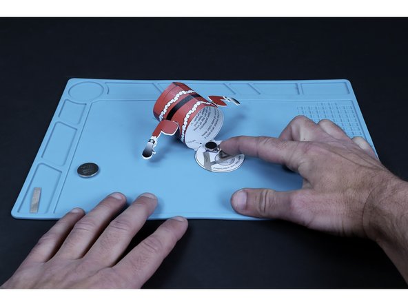 Press the battery atop that tape loop so that the positive (+) side faces UP.