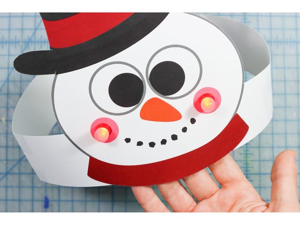 Tape the headband pieces to the sides of the paper as shown. One side's fringe will face up and the other will face down so that you can interlock them as shown.