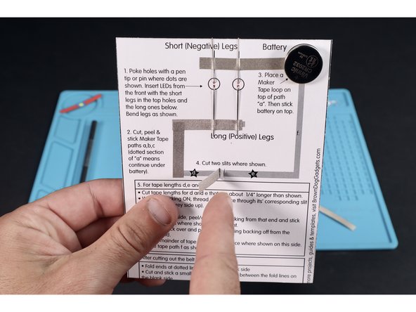 With the backing kept ON, thread the tape section for &quot;d&quot; through its' slot from the back so the backing faces left and the tape faces right as shown.