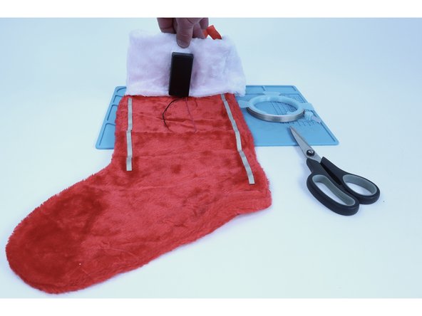 Choose a spot on the back side of the stocking to stick that battery pack to. We have ours pictured near the middle on the cuff but after having assembled it, noticed that its weight would have been better positioned directly behind the hanging loop.