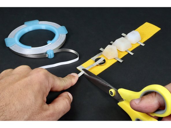 Measure, cut, peel and stick another Maker Tape segment that reaches from the top of the battery all the way to the two overlapping pieces from the previous step.