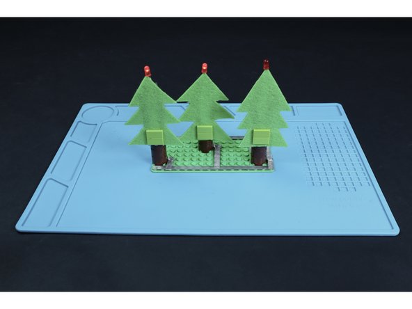Measure, cut, peel and stick one final tape length where shown so that it can be stuck to the top of the battery. This will complete the circuit and turn on all three of your blinking LEDs. Peeling it away from the top of the battery will turn the circuit off.