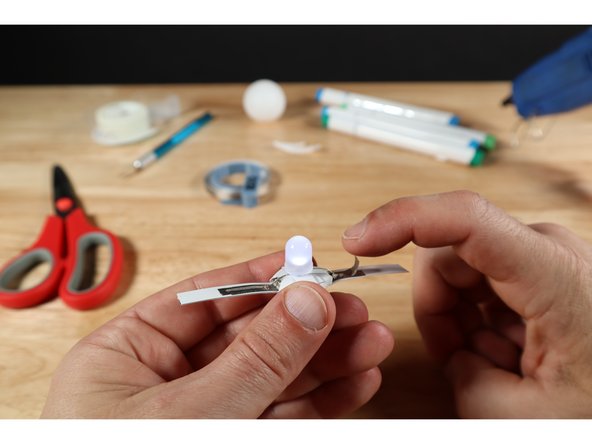 With the LED positioned over the platform created by the battery and the taped leg oriented over the path that connects to the top of the battery, press the leg and tape into contact with the path below ("A.").