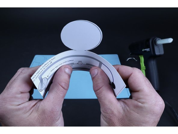 Flatten the LED legs outward in opposite directions so they lay flat against the paper as shown. Now bend them slightly to match the curve that your tube now wants to be shaped as after having curled it earlier.